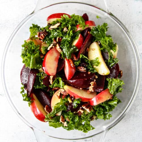 Kale and beet salad with apples in a glass bowl.