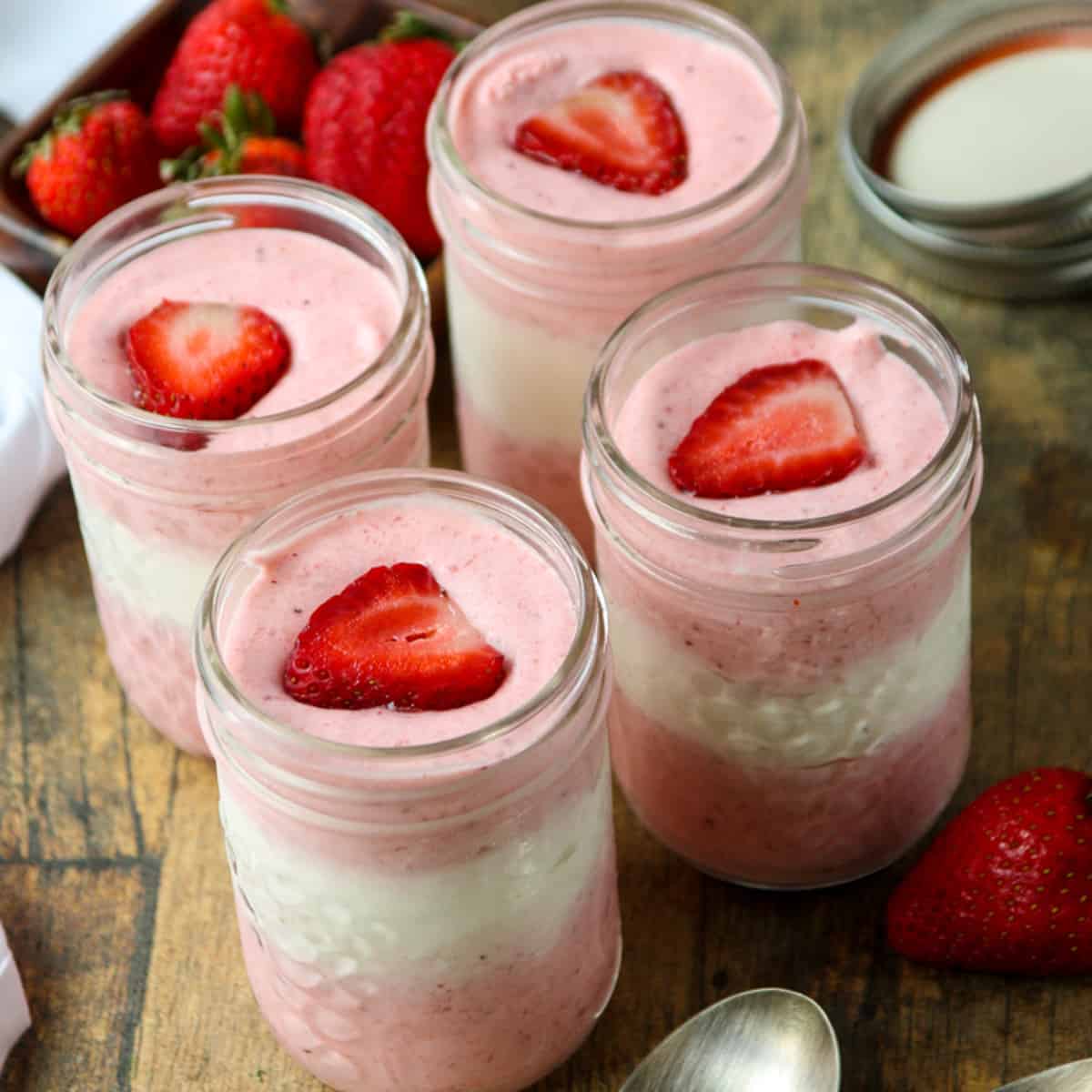 Four jars of strawberry mousse on a wooden table.