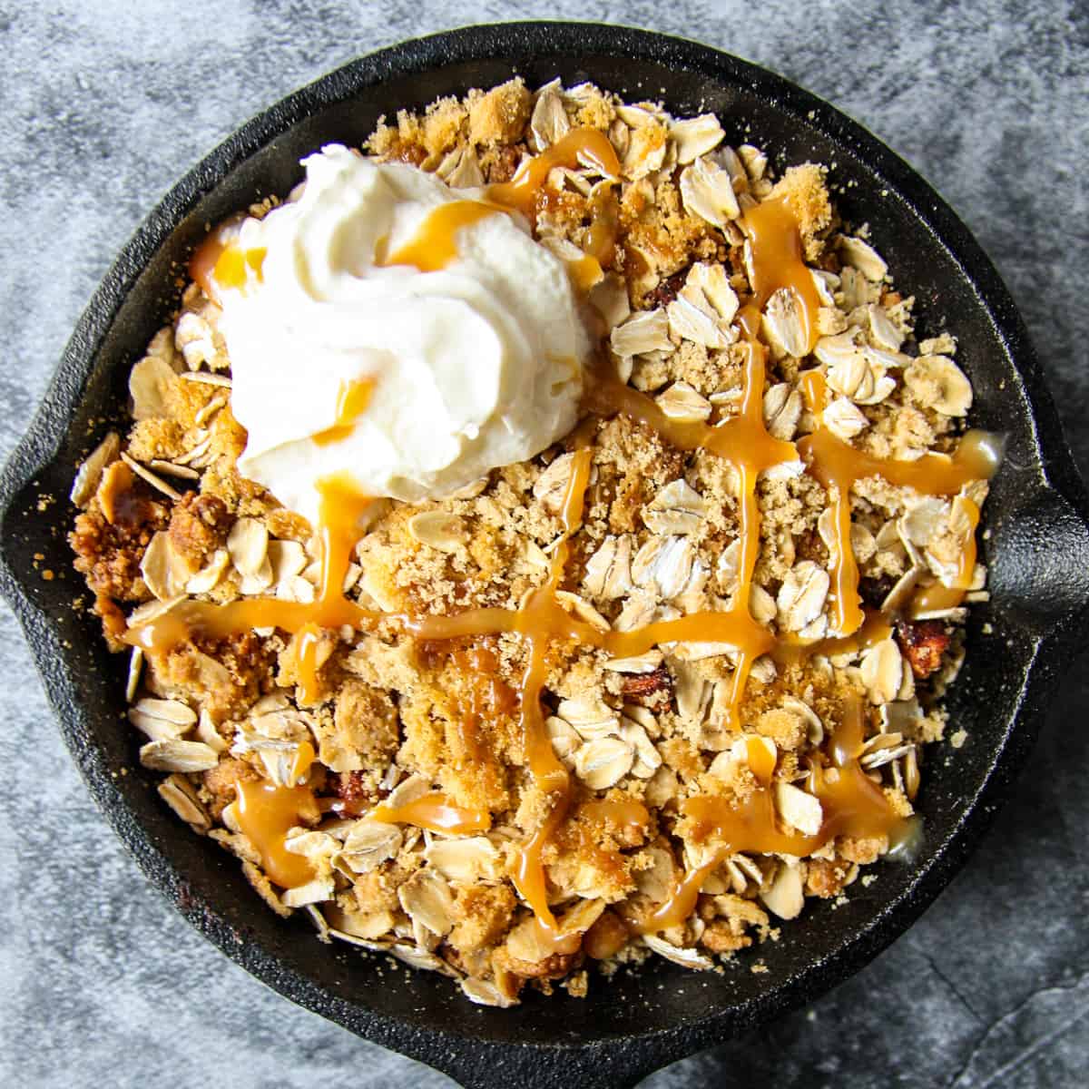 Air fryer apple crisp in a cast iron pan, drizzled with caramel sauce.