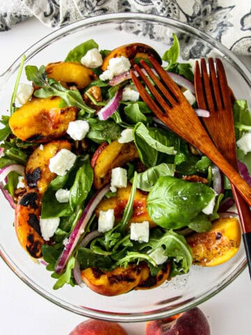 Grilled peach salad in a glass bowl with two wooden forks.